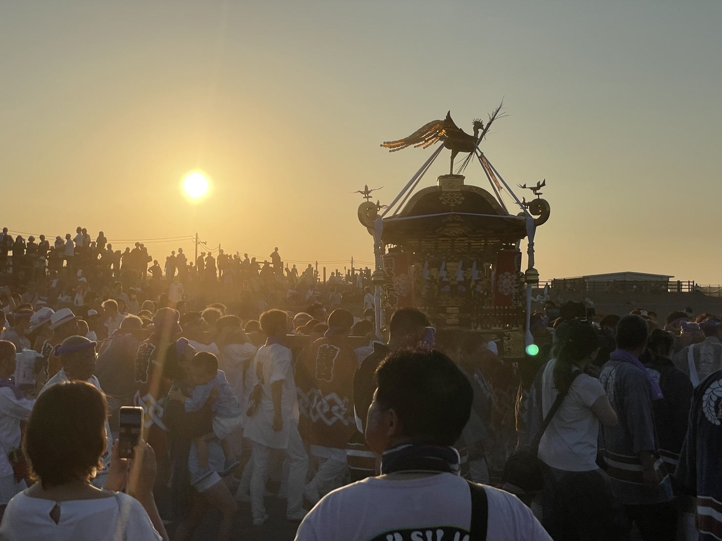 朝日が昇る浜降祭会場で神輿を囲む担ぎ手と観客の様子