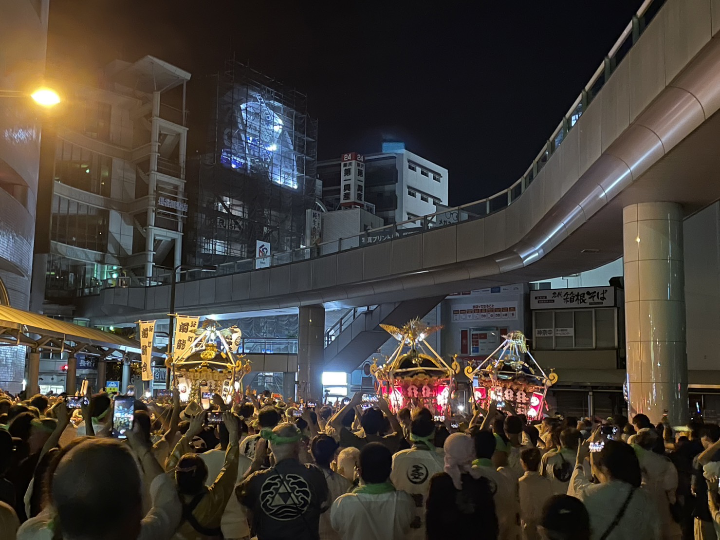 深夜2時の茅ヶ崎駅前で、明かりに照らされた神輿が並び、担ぎ手や観客がスマートフォンで撮影している。北口ロータリーの熱気は最高潮。